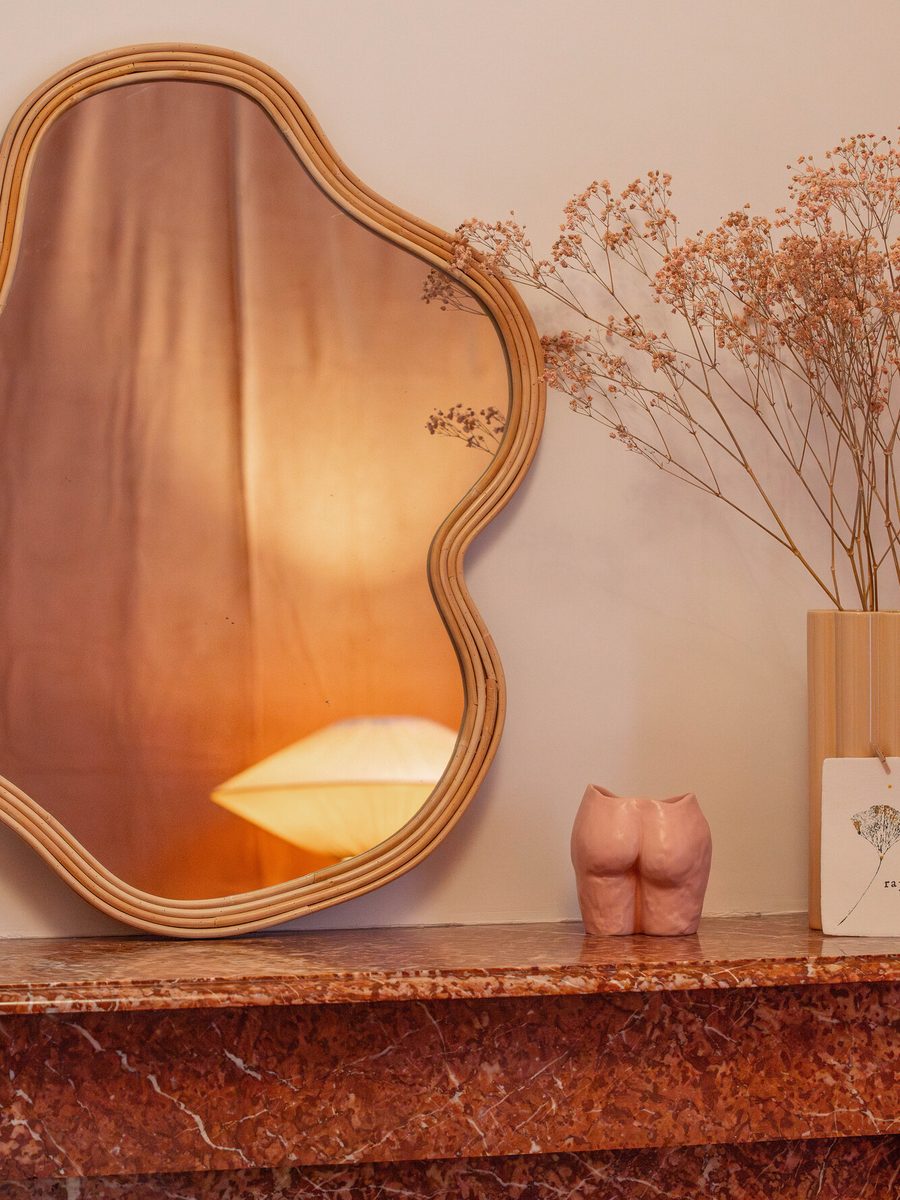 Un miroir ondulé posé sur une cheminée de marbre.